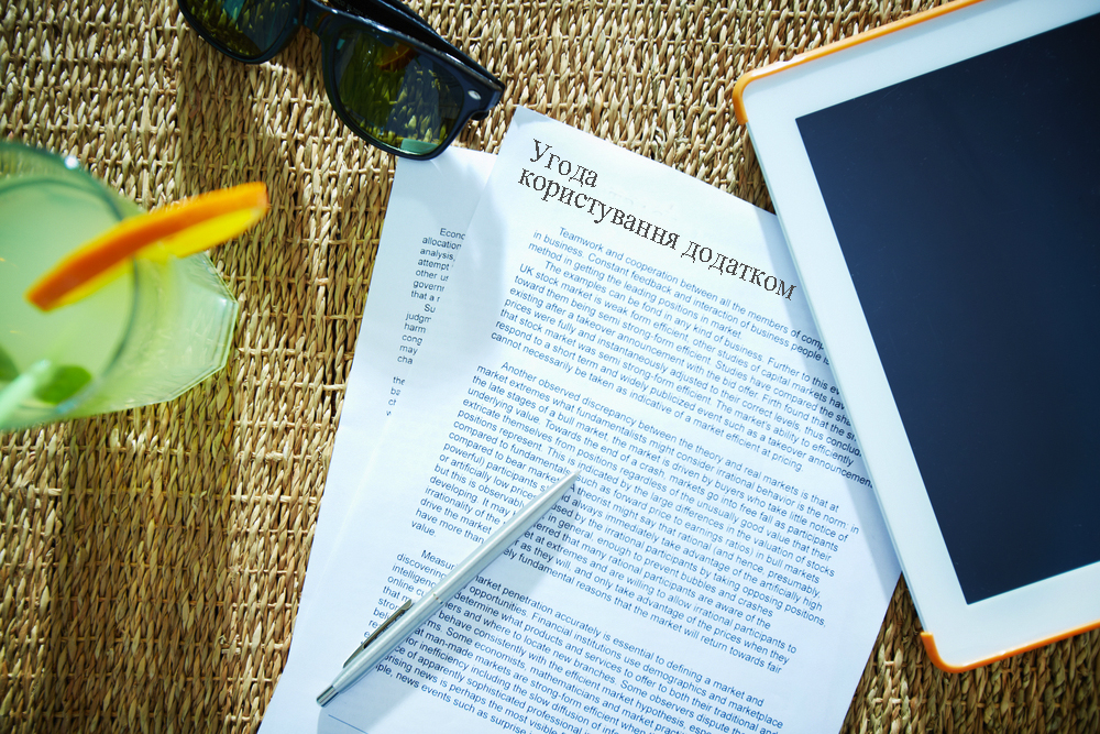 Image of business contract with pen, touchpad, cocktail and sunglasses near by