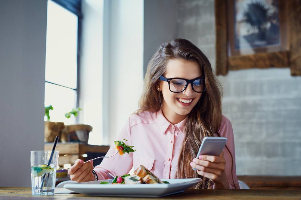 woman eating salad at restaurant and texting on smartphone