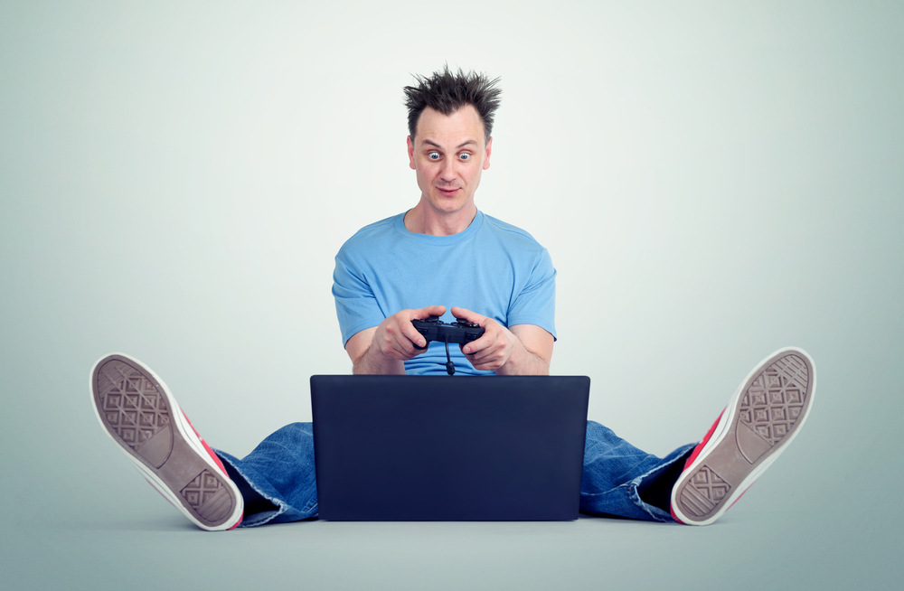 Funny man with a joystick sits on the floor in front of a laptop Gamer plays