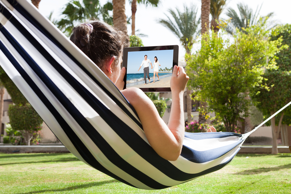 Young Woman Lying In Hammock Watching Video On Digital Tablet