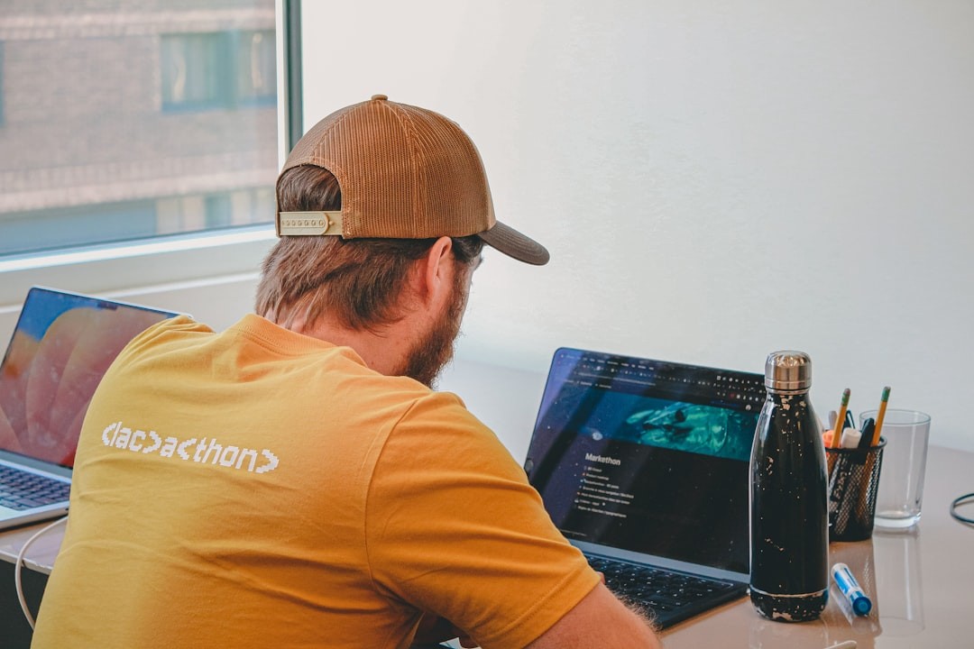 Man in a baseball cap coding on laptops