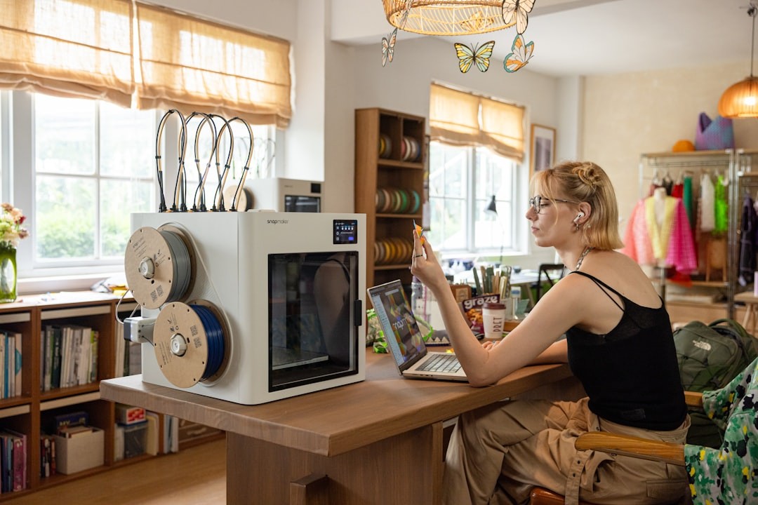 Woman using 3D printer and laptop in workshop