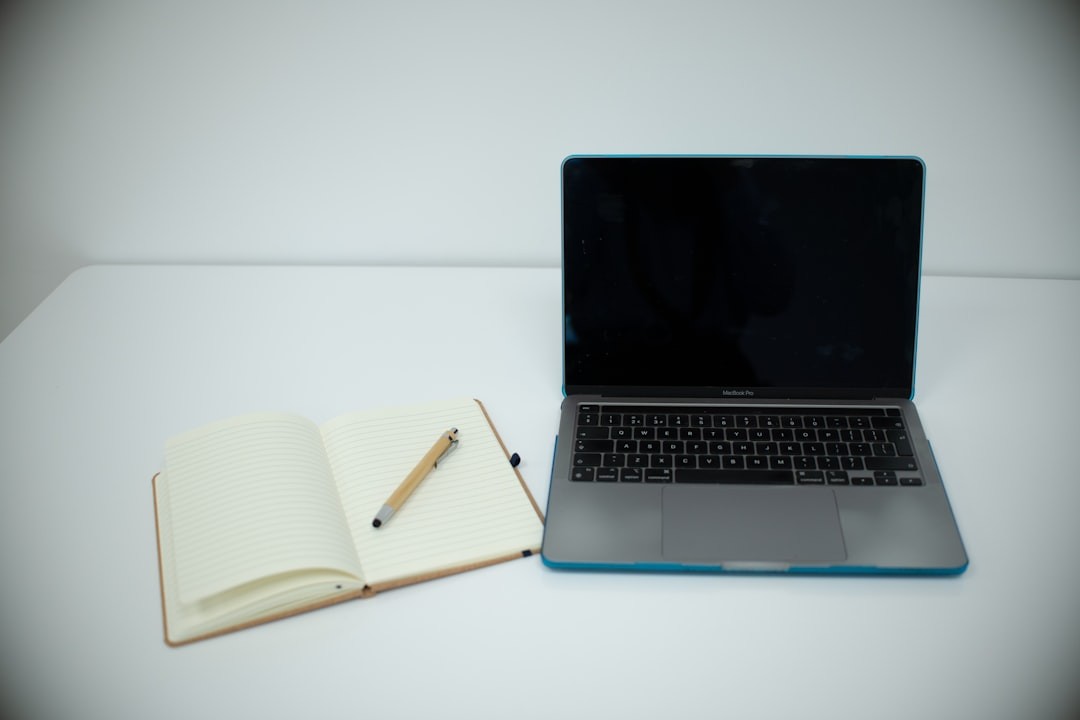 Laptop and open notebook with pen on desk