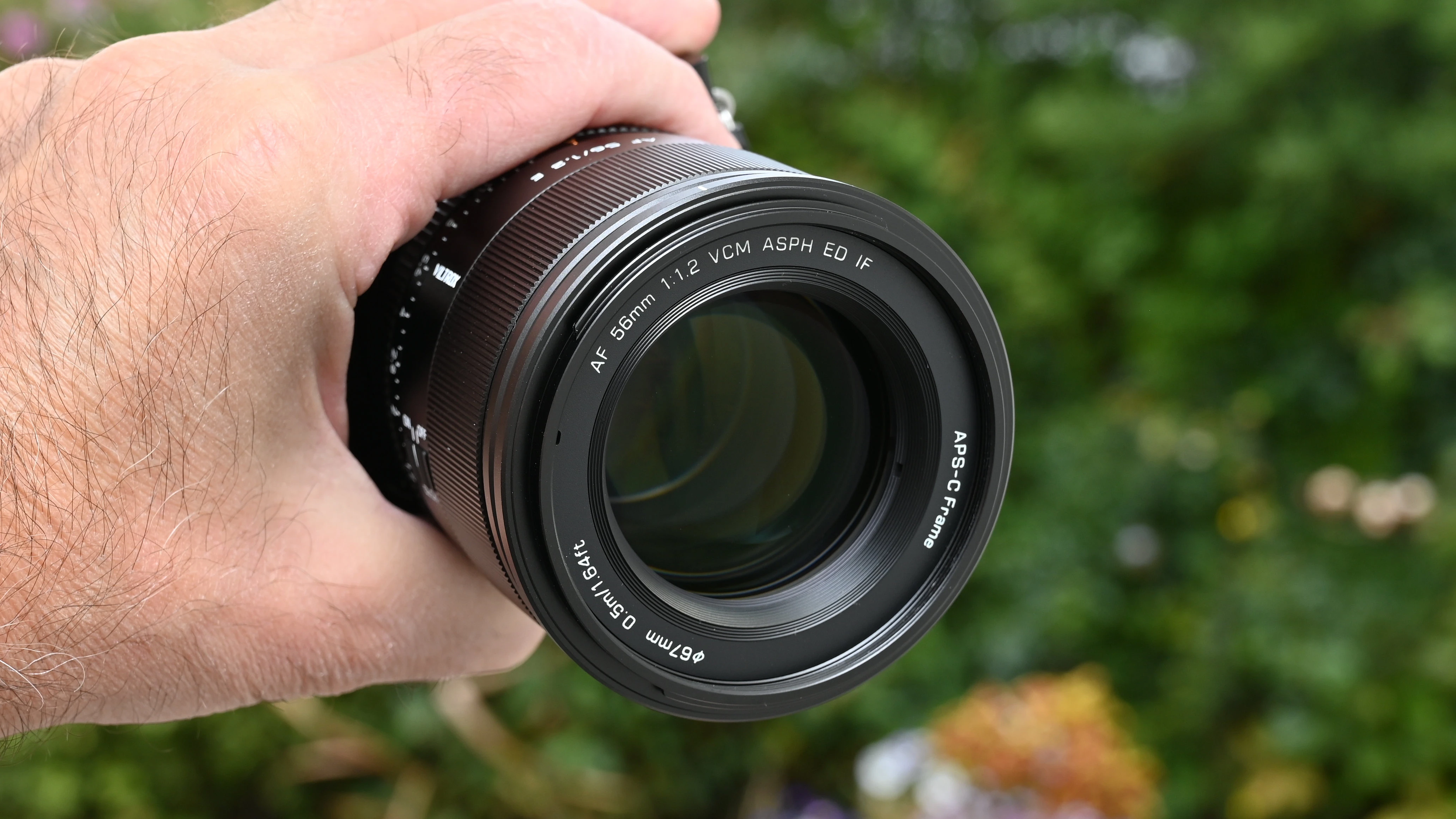 Передня лінза об'єктива Viltrox AF 56mm f/1.2 Pro в руці з видимим маркуванням технологій VCM ASPH ED IF на оправи