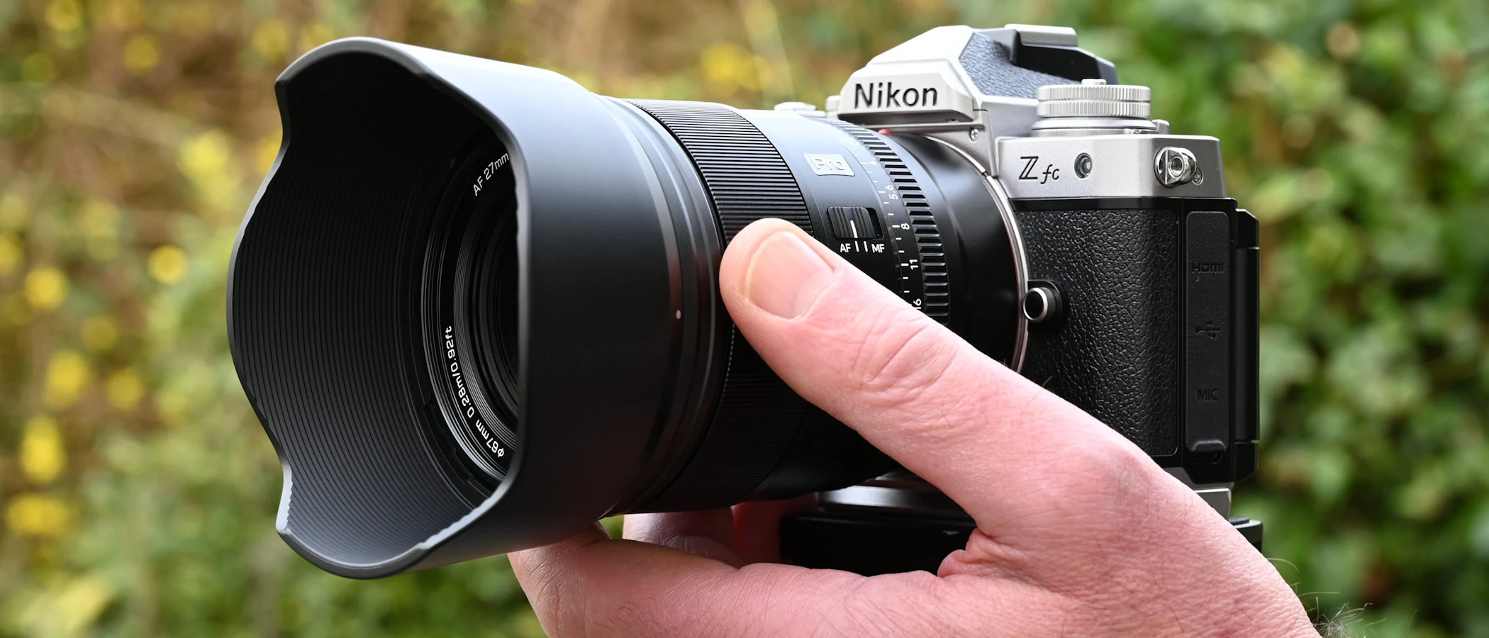 Об'єктив Viltrox AF 27mm F1.2 Pro з пелюстковою блендою на компактній камері в руках оператора на відкритому повітрі