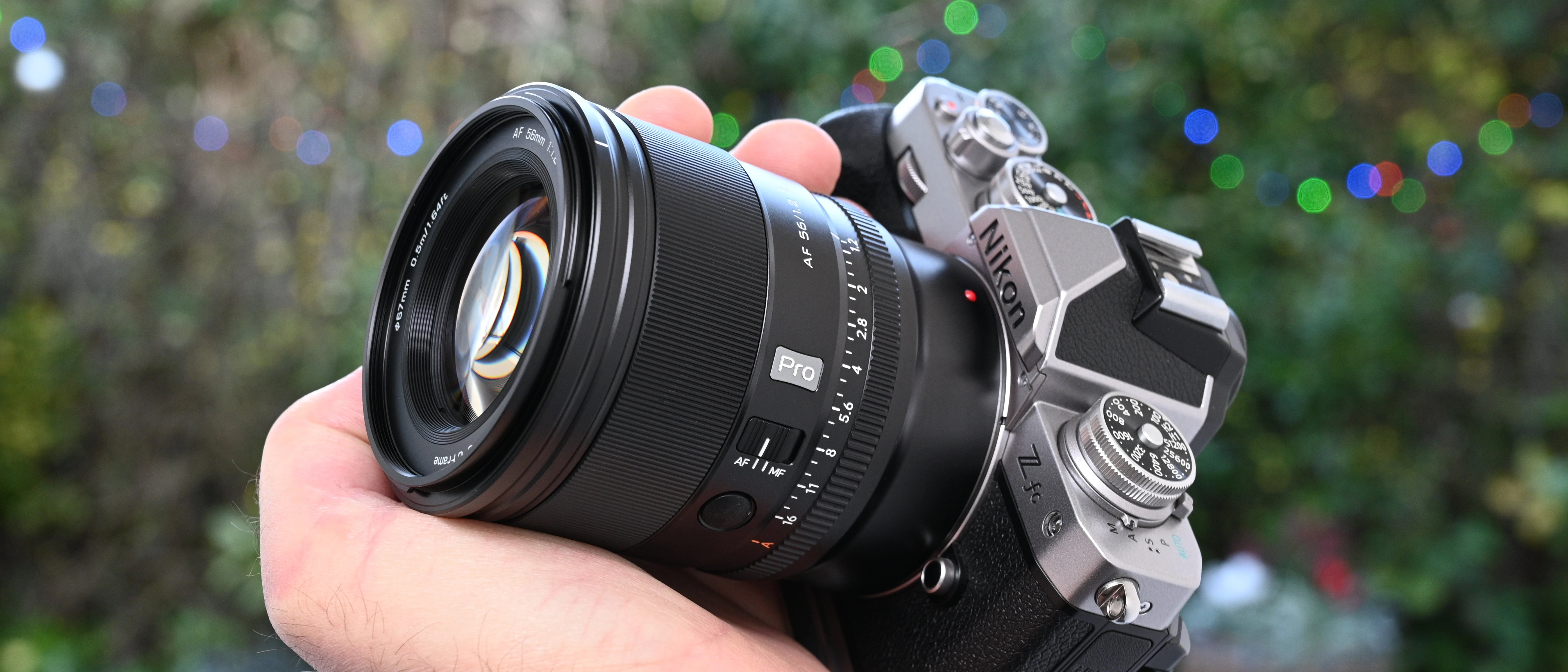 Камера з встановленим об'єктивом Viltrox AF 56mm f/1.2 Pro у руці фотографа на тлі вечірніх вогників боке
