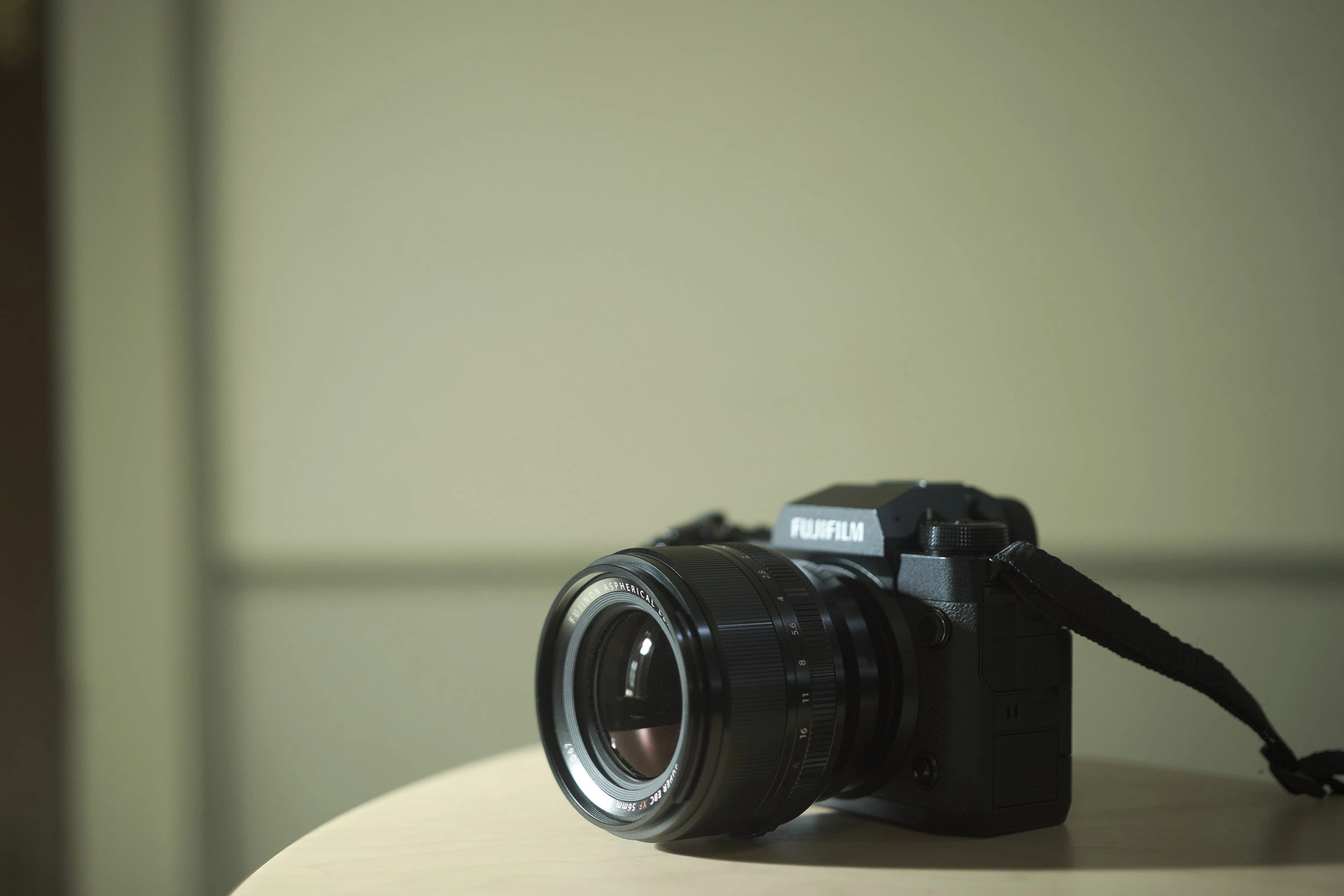 Чорна камера Fujifilm з встановленим портретним об'єктивом Fujinon XF 56mm f/1.2 R WR на дерев'яному столі в кімнаті