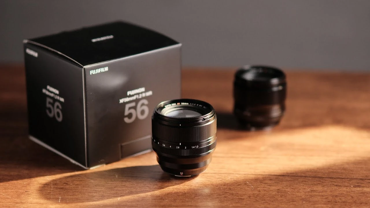 Об'єктив Fujinon XF 56mm f/1.2 R WR поруч з фірмовою коробкою на дерев'яному столі при сонячному світлі